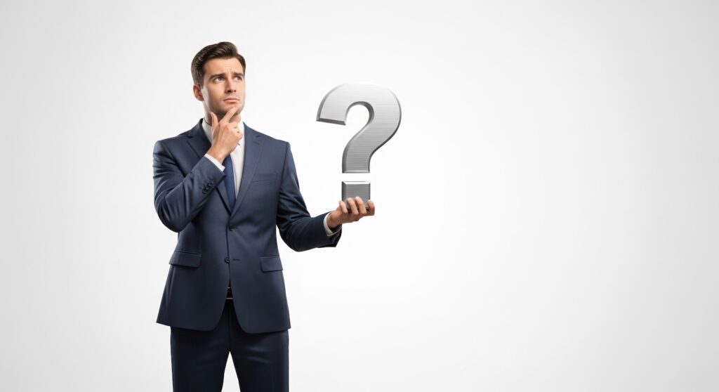 Confused businessman contemplates question mark held in hand, deep in thought. Thoughtful businessman in suit ponders problem, solution, or answer.